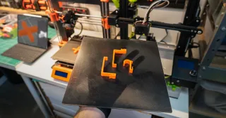 Peças laranja impressas em 3D sobre a placa removida da impressora (foto ilustrativa)