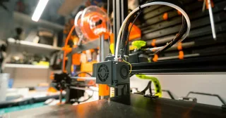 Impressora 3D com carretel de filamento em uma oficina (foto ilustrativa)